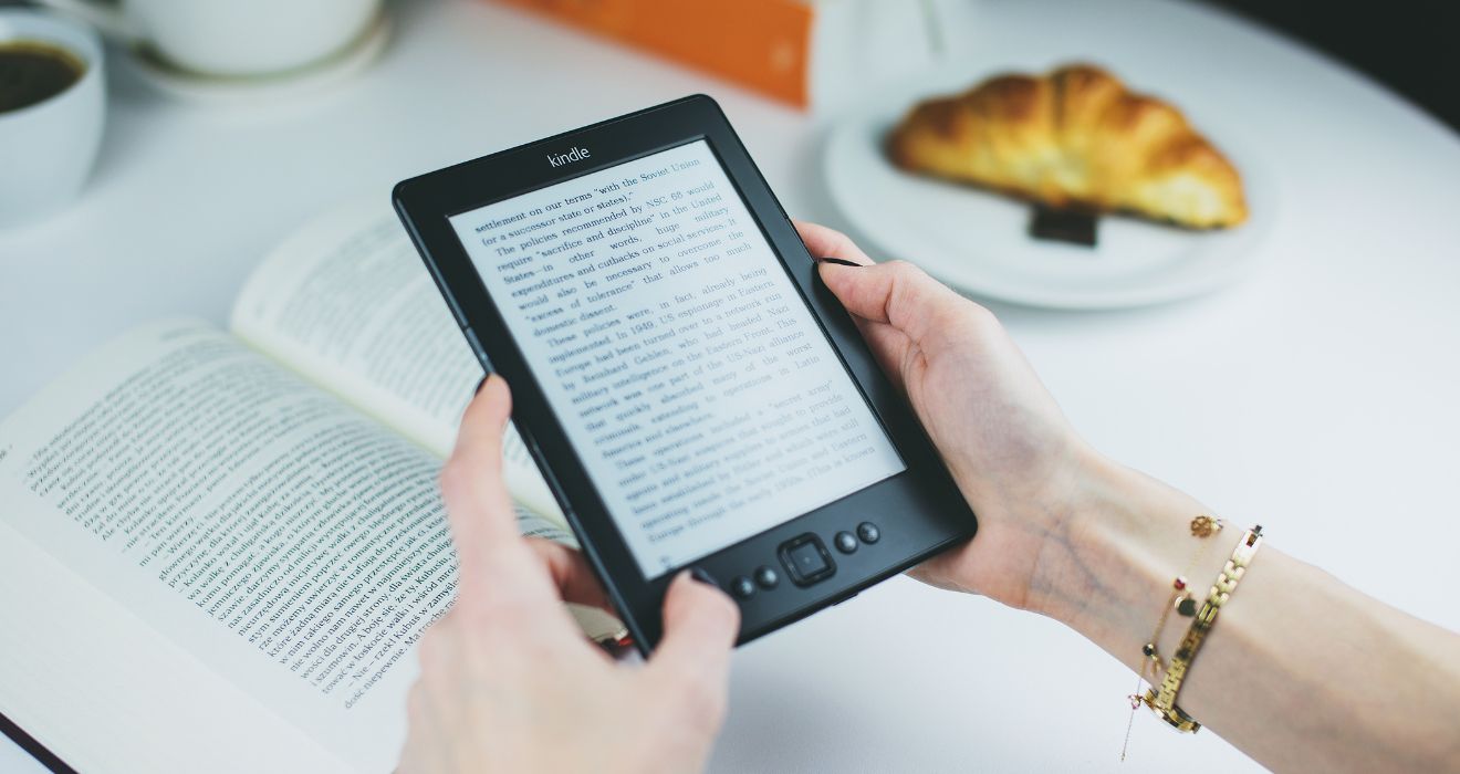 Osoba czyta e-booka na czytniku elektronicznym przy kawie i książce – ilustracja do artykułu o stawce VAT na sprzedaż e-booków